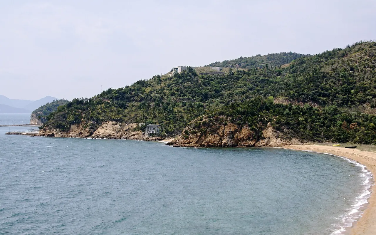 Eine sandige Bucht und eine bewaldete Landzunge an der Küste von Naoshima unterhalb des Museums