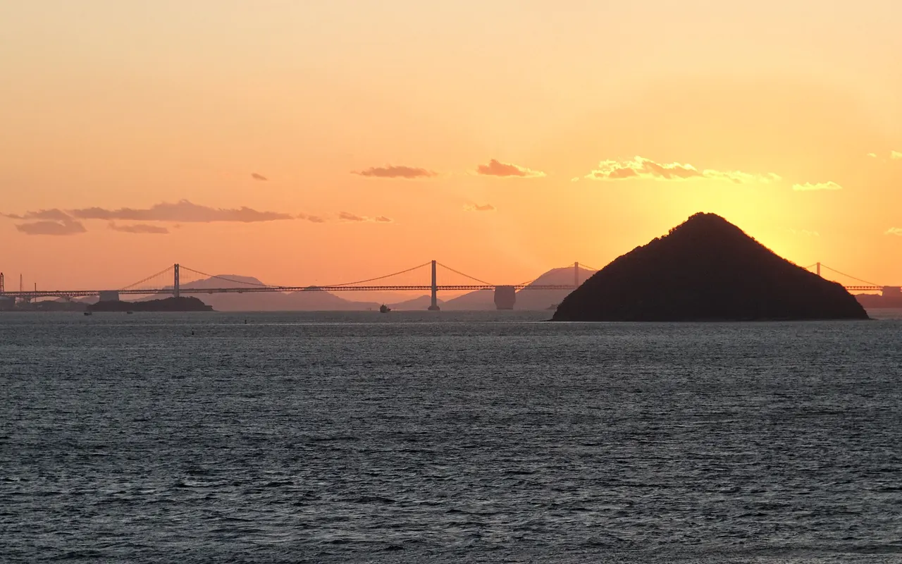 Sonnenuntergang über der Seto-Inlandsee mit einer kegelförmigen Insel und einer langen Hängebrücke am Horizont